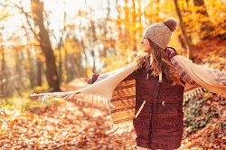 female in warm clothes walking through fallen leaves